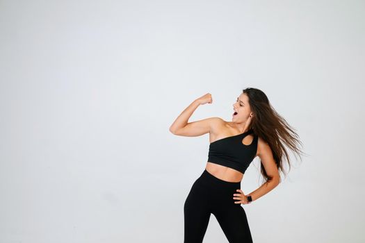 Cheerfully beautiful smiling sporty woman demonstrating biceps, isolated on white background.