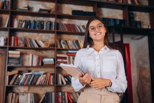 Young woman with documents on the background of a bookshelf