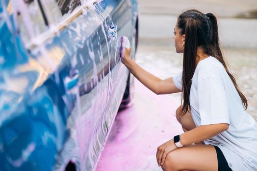Woman with two pigtails with a sponge washes the side of the car