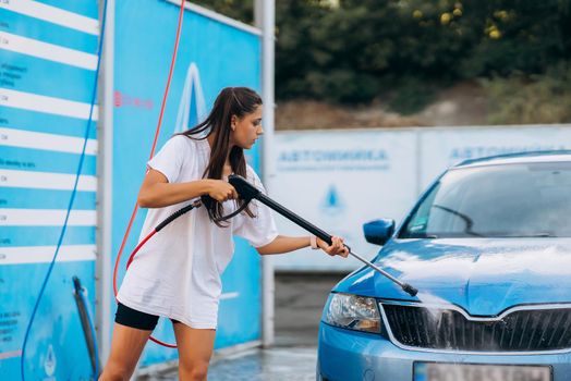 Brunette with two pigtails from a high-pressure hose washes the car at a car wash