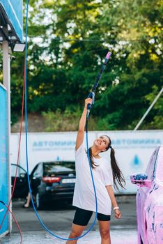 Woman with high pressure hose stands by car