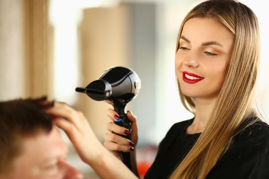 Woman hairdresser doing styling with hairdryer to man. Training men's hairstyles concept