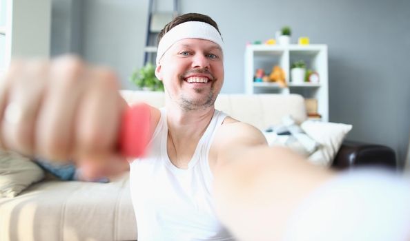 Young man doing exercises with dumbbells smiling at camera. Home fitness and sport concept