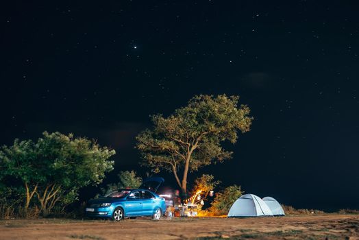 Group of five travellers rest on sea shore under tree on blue evening sky background. Tourism and camping concept.