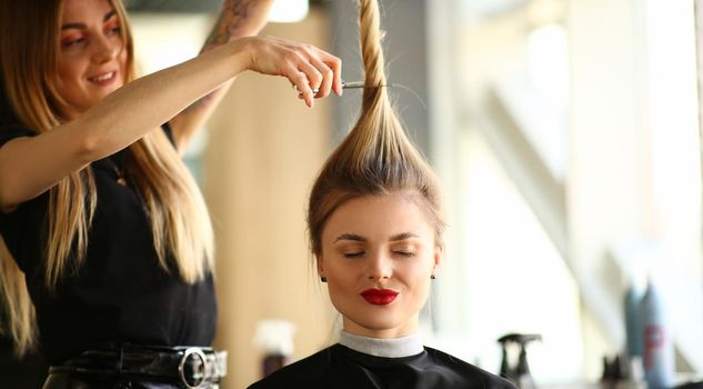 Woman hairdresser holds a client ponytail and scissors. Beauty salon services and trendy haircuts concept