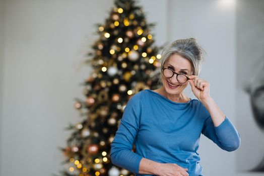 Elderly lady smiling and looking in camera, Xmas tree sparkling on background