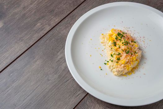 Still life of ensaladilla rusa with potatoes and egg and olive oil sauce on a white plate on a wooden board. Traditional Spanish gastronomy concept.