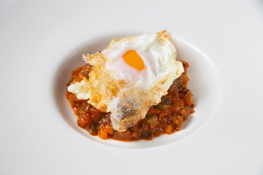 Close-up still life of ratatouille with fried egg on a white plate. Concept of traditional Spanish gastronomy.