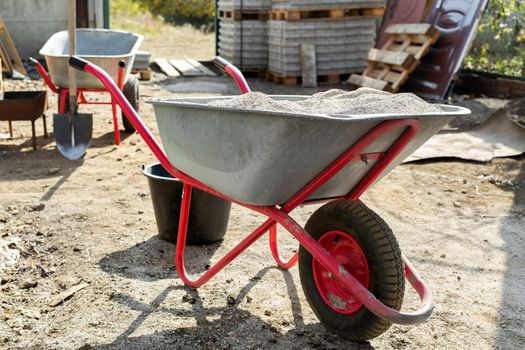 Construction wheelbarrow with cement and a shovel on the background of a stack of gray tiles.