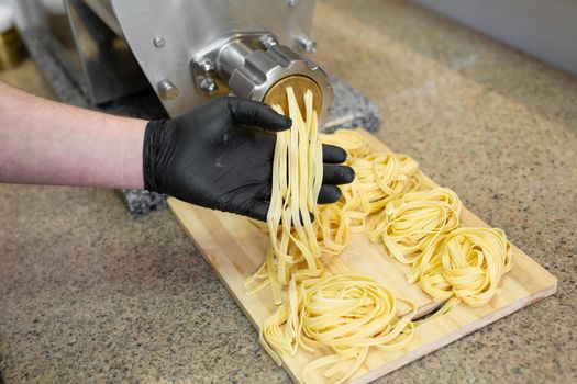Pasta, noodles come out of a professional machine, cook opens it and twists it on a wooden board.