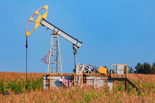 The old oil pump in a field under blue sky