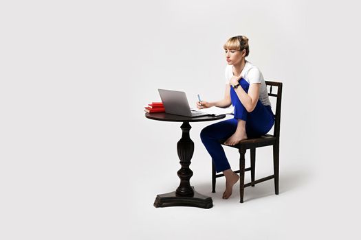 Focused young woman sitting at desk working or studying remotely writing notes while looking on the notebook laptop screen. Distant learning or remote work concept. Isolated on white background.