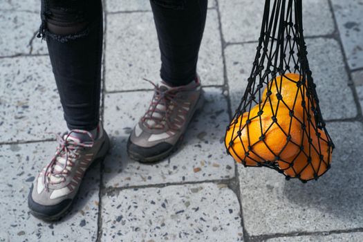 Woman carrying mesh bag of fresh oranges on the street