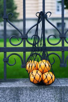 Black mesh bag full of oranges as a symbol of zero waste lifestyle is hanging on the wrought iron fence. Forgotten item.