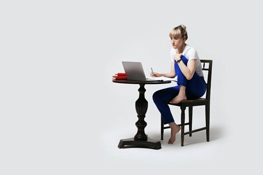 Focused young woman sitting at desk working or studying remotely writing notes while looking on the notebook laptop screen. Distant learning or remote work concept. Isolated on white background.