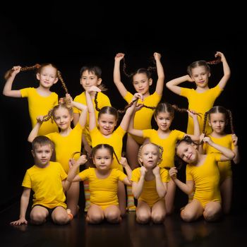 Group of little children dancers posing in studio. Boys and girls in yellow sportswear posing against black background. Dance school, kids education concept