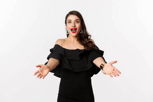 Fashion and beauty concept. Happy young woman in glamour black dress, reaching hands forward to take something, waiting for hug, white background.
