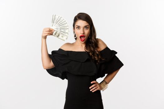 Beauty and shopping concept. Fashionable woman with red lips, showing dollars and smiling, standing over white background with money.