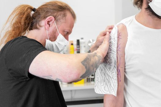Skilled Tattoo artist putting a sketch on the arm of a man. High quality photo