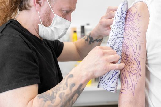 Skilled Tattoo artist putting a sketch on the arm of a man. High quality photo