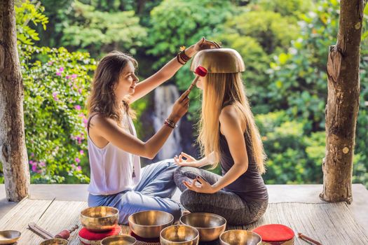 Nepal Buddha copper singing bowl at spa salon. Young beautiful woman doing massage therapy singing bowls in the Spa against a waterfall. Sound therapy, recreation, meditation, healthy lifestyle and body care concept.