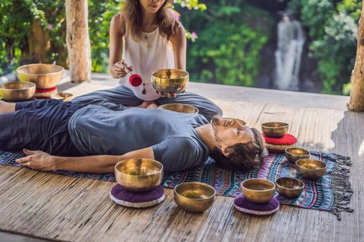 Nepal Buddha copper singing bowl at spa salon. Young beautiful man doing massage therapy singing bowls in the Spa against a waterfall. Sound therapy, recreation, meditation, healthy lifestyle and body care concept.