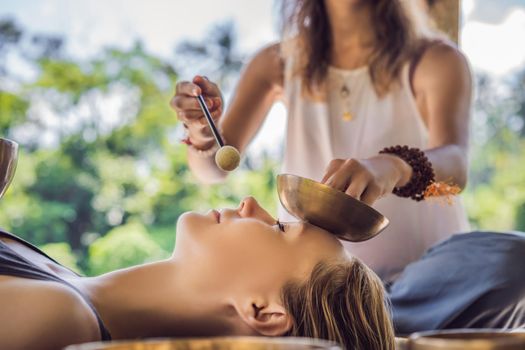 Nepal Buddha copper singing bowl at spa salon. Young beautiful woman doing massage therapy singing bowls in the Spa against a waterfall. Sound therapy, recreation, meditation, healthy lifestyle and body care concept.