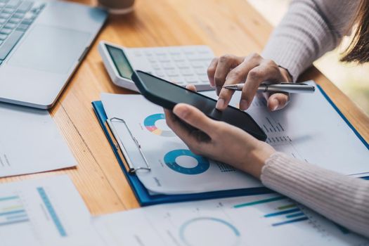 Close up woman hold smartphone for project stats financial data sales charts on laptop and cellphone screen at workplace.
