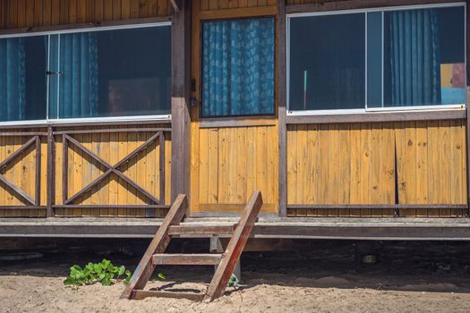 Outside view facade. Wooden yellow brown boards material, country house, panoramic window glass nature reflect, curtains inside. Summer day warm light mood. Cozy home interiors, leisure, eco building.