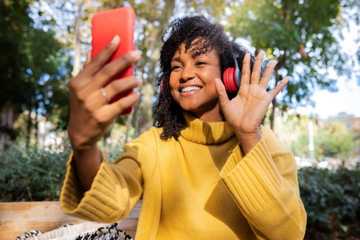 Smiling young African American woman wave hand on video call using mobile phone outdoors. Lifestyle and technology concept.