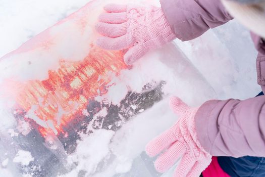 child's hands in knitted gloves on a glowing ice cube.