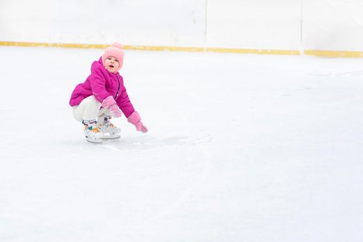 kid girl in a red jacket skates on a skating rink