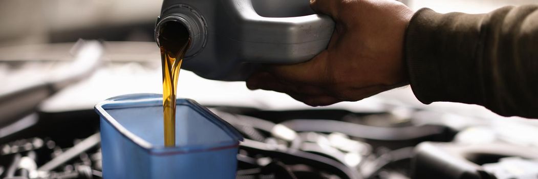 Foreman pours car oil into engine through watering can. Engine oil change intervals concept