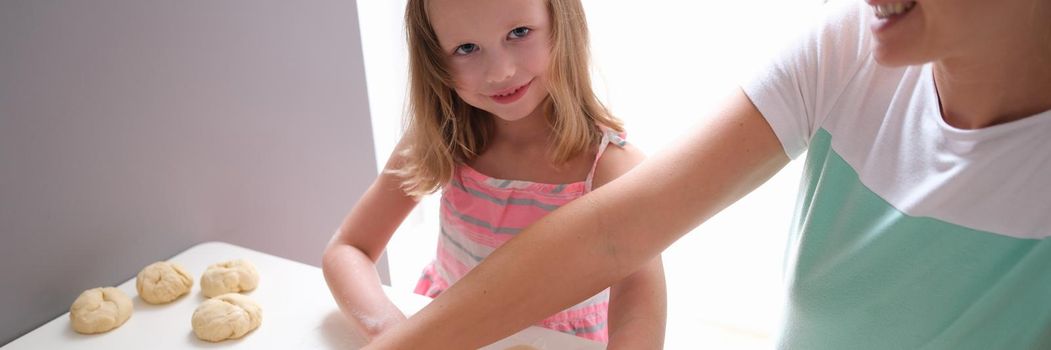 Smiling mother and daughter roll out dough with rolling pin. Cooking sweet food together with children concept