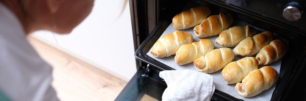 Woman takes out baking sheet of cooked croissants from oven. Cooking flour products at home concept