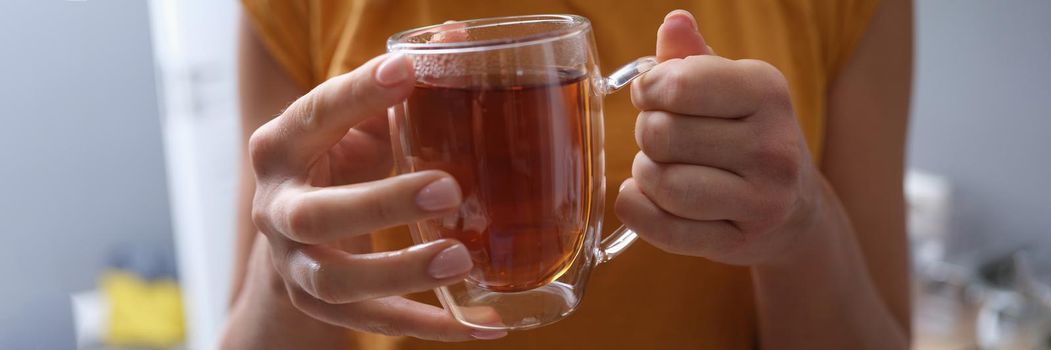Woman holds transparent cup of hot tea in hands. Tea selection concept