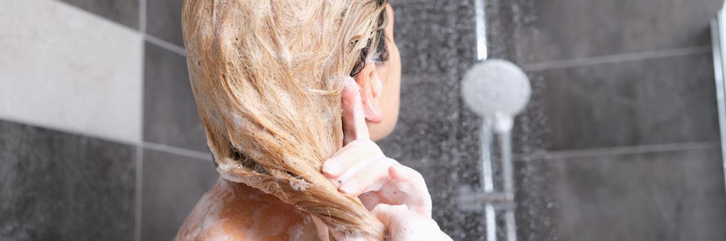 Woman washes hair with shampoo in shower. Hair care concept