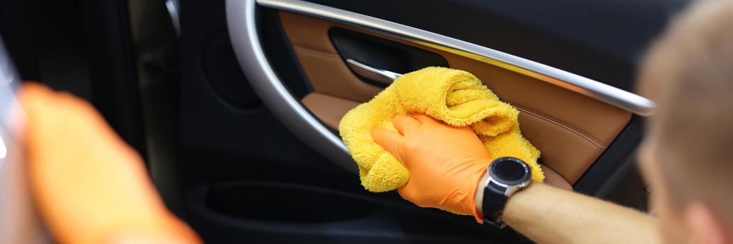 Gloved handyman wipes car doors inside cabin. Car wash services for car maintenance concept