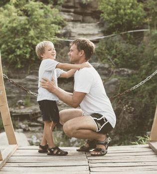 Vintage matte effect photo. Happy lifestyle moment. Man crouched, gesture hand, attentive listen boy walk funny play. Father hug hold touch child son closely in arm embrace, fatherhood love affection