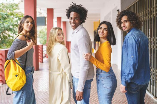 Side view of group of content multiethnic friends standing in street and looking at camera while enjoying stroll in summer