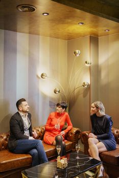 Company of glad friends wearing elegant outfits sitting at table in posh restaurant and drinking champagne while celebrating event together