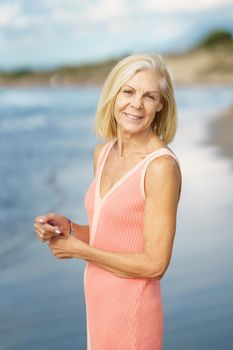 Beautiful mature woman walking along the shore of a tropical beach, wearing a nice orange dress. Elderly female enjoying her retirement at a seaside retreat.