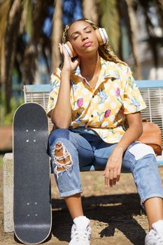 African woman with skateboard. Black girl relaxing after riding skateboard listening to the music outdoors.