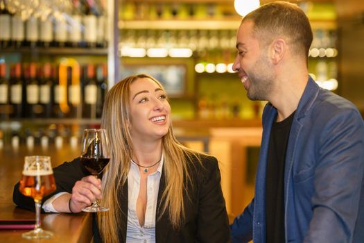 Cheerful multiracial man and woman with alcohol drinks smiling and looking at each other while having date in bar