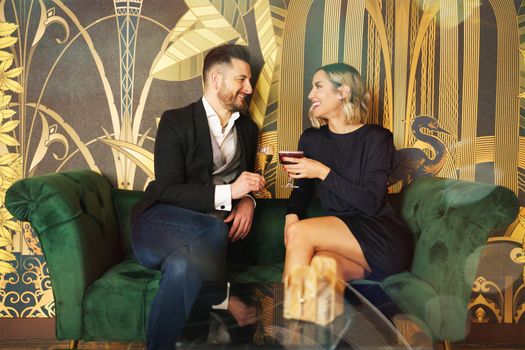 Loving middle aged couple on couch with drinks on coffee table in hotel lobby. Elegantly dressed man and woman enjoying their romance.