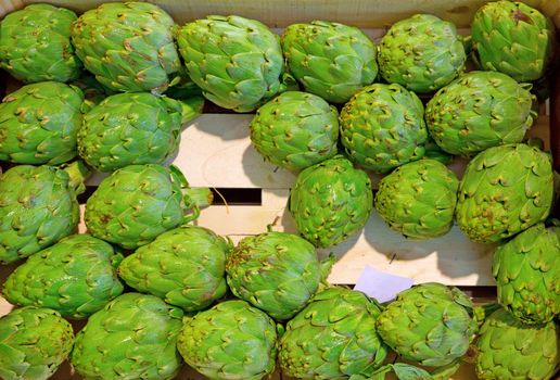 many artichokes for sale on the market over wooden box