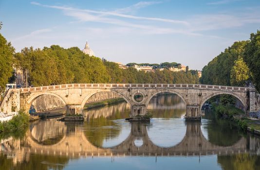 ROME, ITALY - CIRCA AUGUST 2020: Bridge on Tiber river with Vatican Basilica cupola in background and sunrise light.