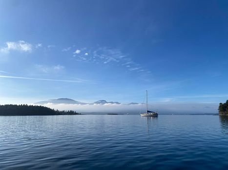 A single sailboat at anchor with calm water and blue skies, Gulf Islands, British Columbia Canada