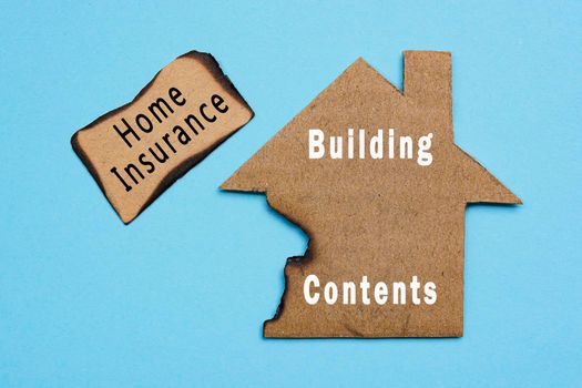 Home insurance, building and contents text on burned paper house model on blue background. Home insurance concept. Flat lay. Directly above.