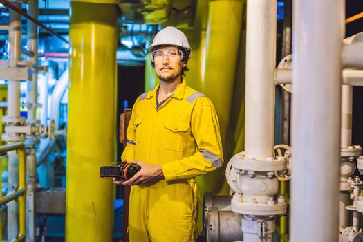 Young man in a yellow work uniform, glasses and helmet in industrial environment,oil Platform or liquefied gas plant.